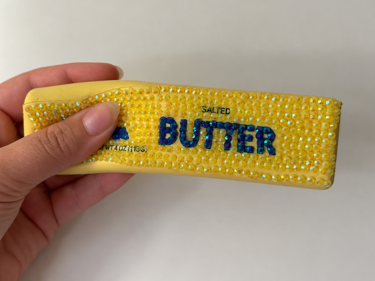 Hand holding a finished butter squishy bedazzling kit covered in yellow and blue rhinestones