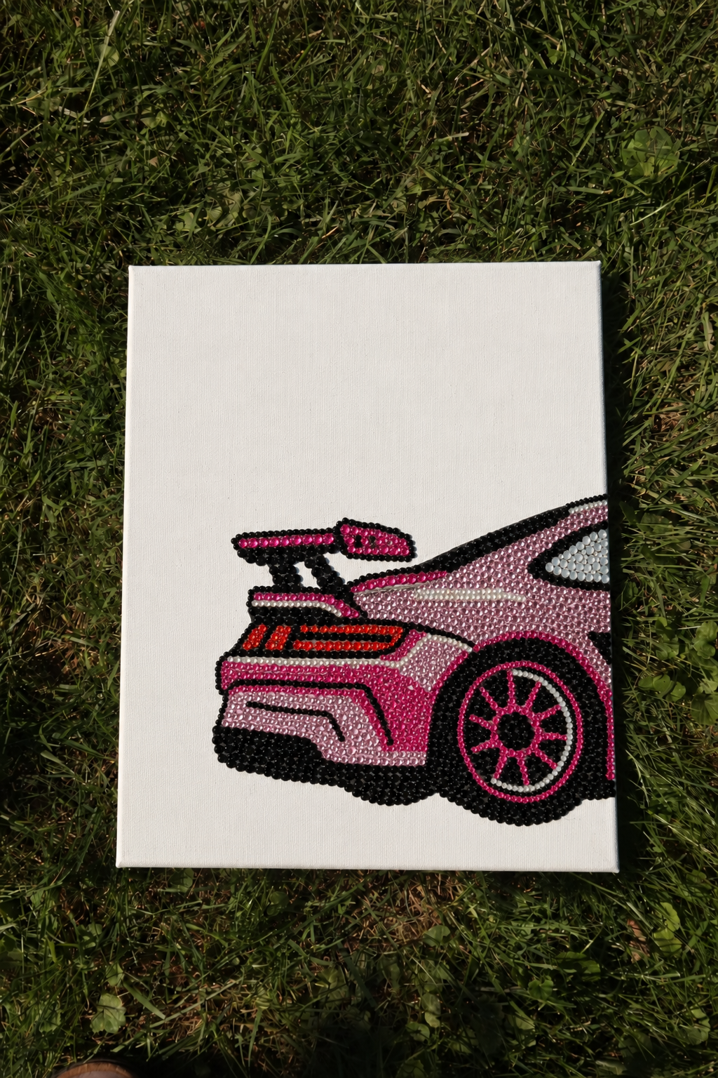 Pink Porsche DIY rhinestone art kit canvas laid on grass, completed design in pink, red and black stones